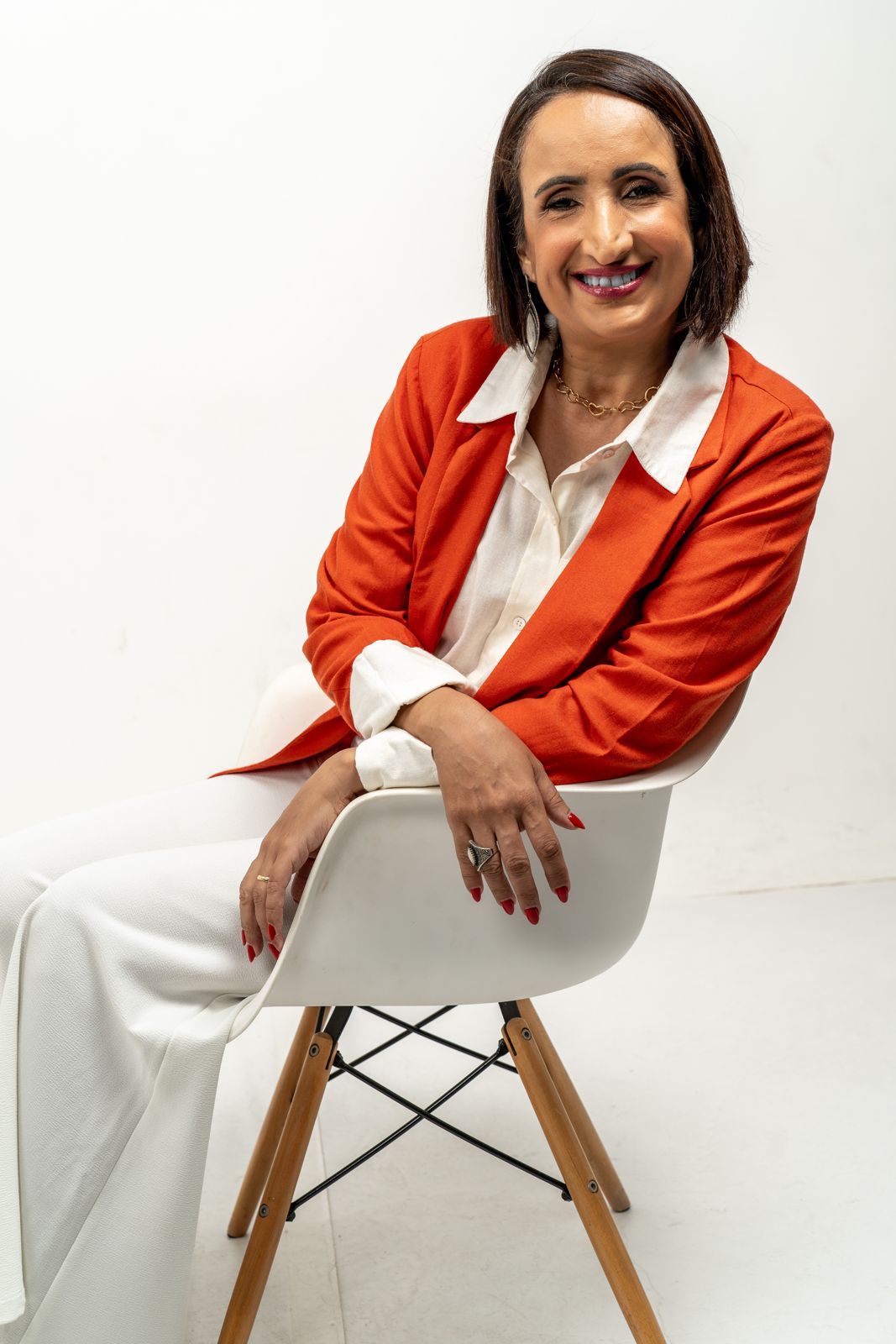 Mônica Borges sentada, de blazer laranja, sorrindo